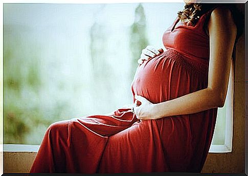 Pregnant woman in a red dress holding her tummy