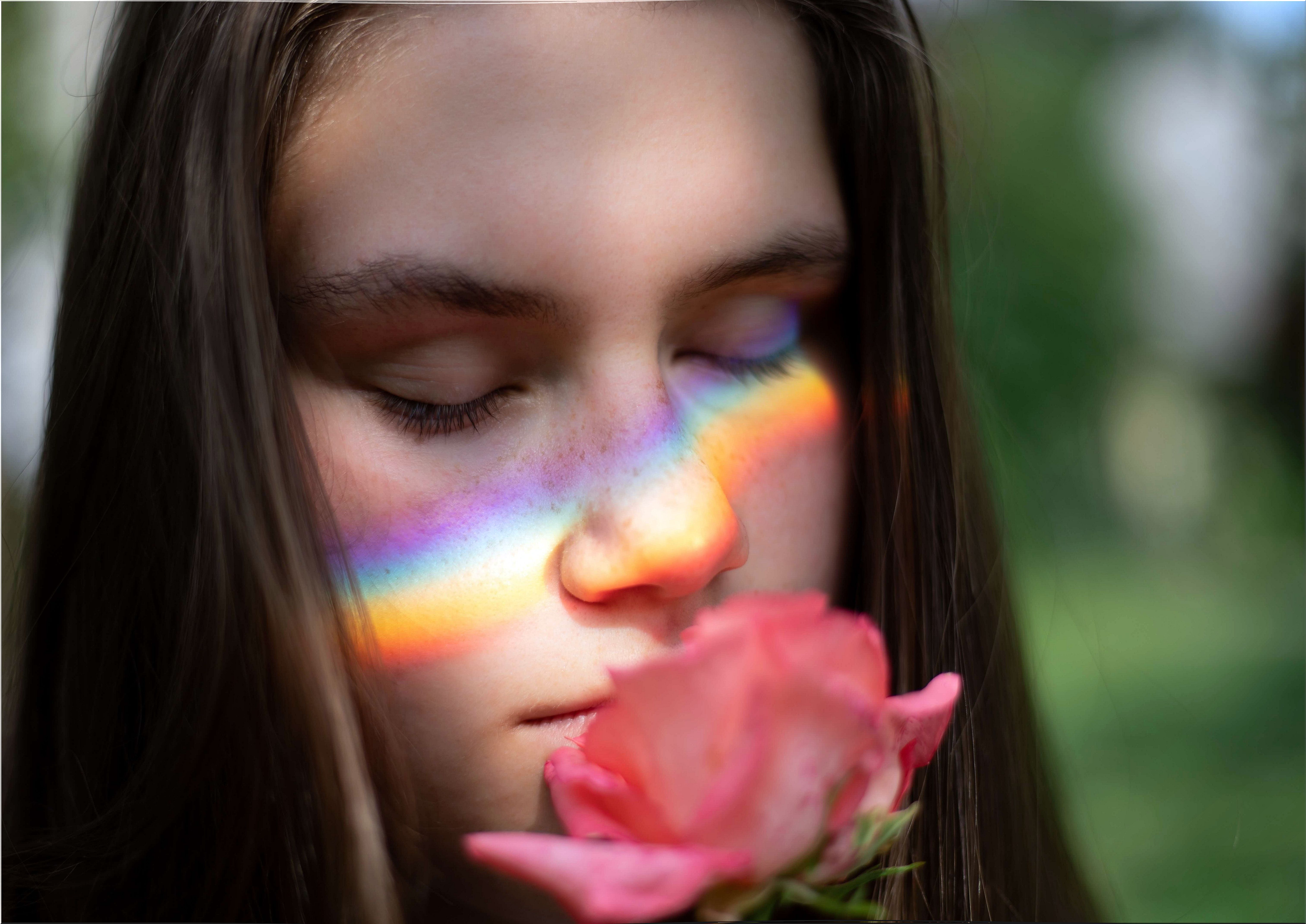 Woman smelling a rose with rainbow reflection on her cheeks and thinking about yesterday's memories